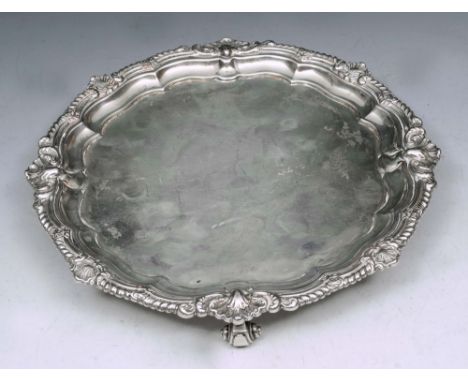 A GEORGE V SILVER SALVER with a shell and scroll border and standing on four scroll feet, 22cm diameter, London 1912 by Carri
