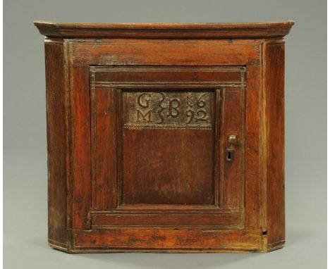 A William & Mary joined oak hanging corner cupboard, with moulded cornice above a panelled door carved with initials and date