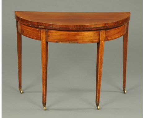 A George III mahogany demi-lune turnover top card table, raised on tapered legs of square section terminating in brass castor