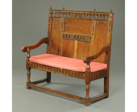 A 17th century joined oak settle, carved and dated "1672", with panelled back, downswept arms, solid seat with cushion and ra
