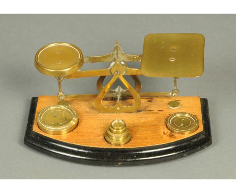 A Victorian brass postal scale, set on a bowfronted ebonised wooden stand.  Width 23 cm. 