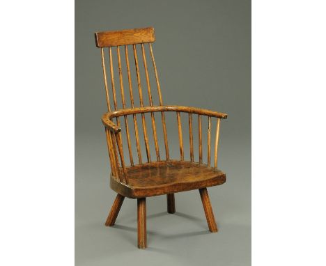 An antique Welsh primitive comb back elbow chair, with narrow tapering back with bowed top rail, spindled supports, solid sea