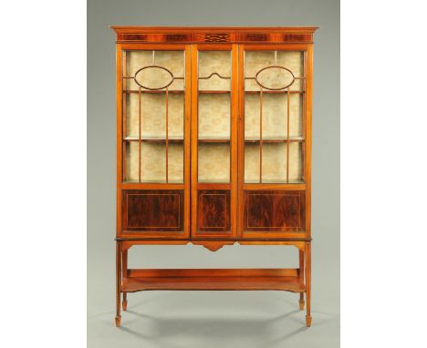 An Edwardian inlaid mahogany display case, with three quarter glazed doors, tapered legs with low shelf and with spade feet. 