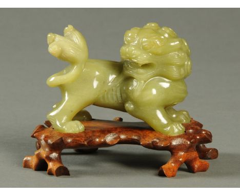 A Chinese jade model temple lion, raised on a carved wooden base.  Length 13 cm. 