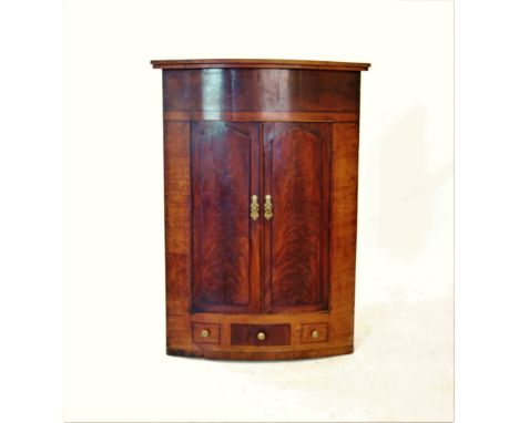 A 19th century mahogany bow front hanging corner cupboard, with a moulded cornice above a pair of panelled doors, enclosing t