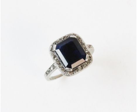 An Art Deco sapphire and diamond cluster ring, the central octagonal step cut sapphire measuring 10mm x 8mm, claw set to a su