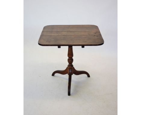 A George III oak tilt top tripod table, the square top with rounded corners, raised upon a ring turned baluster shaft with th