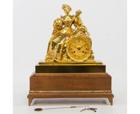 An ormolu gilt table clock on a wood base, with a female figurine holding flowers. Clock with half-hour strik and silk rope s