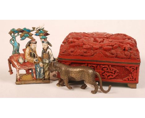 A Chinese carved and stained ivory panel showing an opium smoker seated at an outdoor table, sprung folding gilt metal stand.