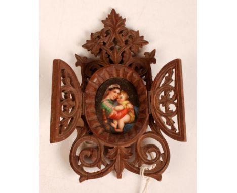 An oval icon of the Madonna and child enamelled on porcelain, the plaque set within a Swiss carved easel stand behind two hin