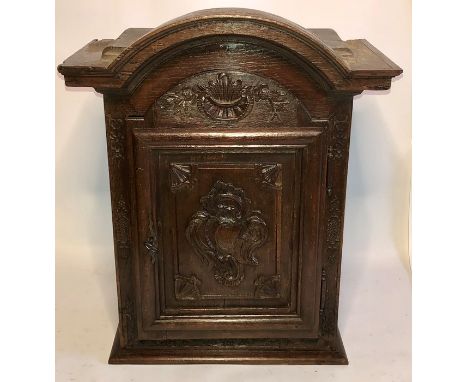 A 17th Century French oak sacristy cabinet, an arch moulded top above a carved single panel door in floral decoration, on a p