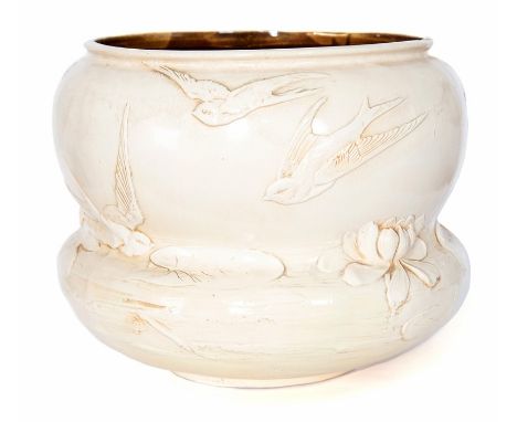 A large waisted Bretby Art Pottery moulded ivory ground jardiniere with moulded decoration of swallows flying above water lil