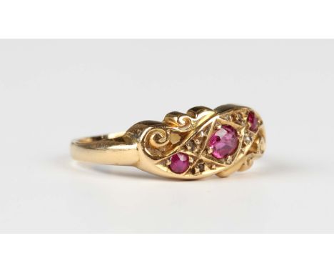 An 18ct gold, ruby and diamond ring in a scroll design, mounted with the principal cushion cut ruby to the centre, Birmingham