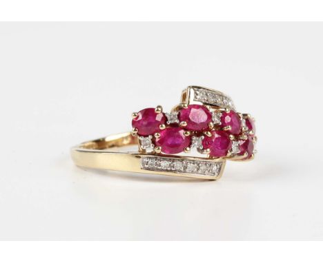 A 9ct gold, ruby and diamond ring, claw set with seven oval cut rubies, otherwise set with circular cut diamonds in a twist d