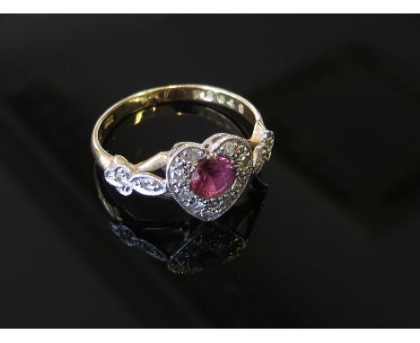 A gold ring of heart form, the central ruby framed by diamonds with diamond set shoulders, size P, 3.5g