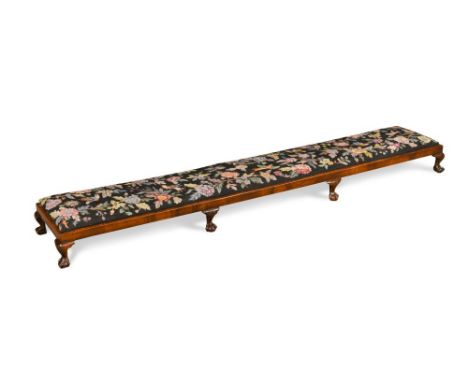 An Edwardian mahogany long foot stool, with needlepoint upholstered drop-in seat and on shell carved cabriole legs and claw a