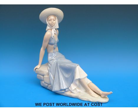 A Nao figurine of a girl in a sunhat reclining on a rock (29cm tall)