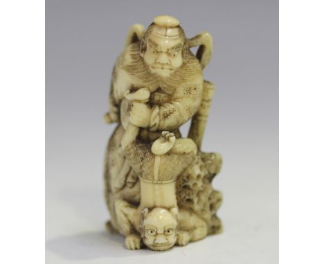 A Japanese carved ivory okimono netsuke, Meiji period, modelled in the form of Shoki the demon-queller holding an oni upside 