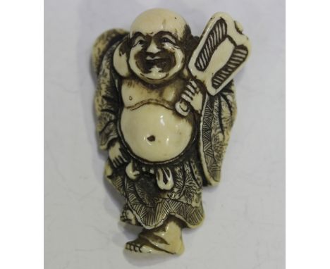 A Japanese carved and stained ivory netsuke by Masahori, Meiji/Taisho period, carved as Hotei holding a fan and standing on o