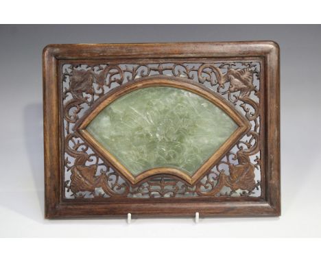 A Chinese spinach green jade fan shaped panel, early 20th century, carved in low relief with pavilions in a mountainous coast