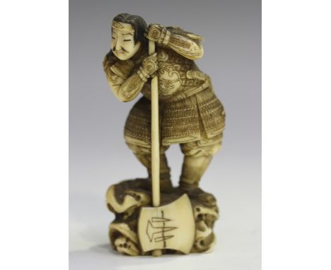 A Japanese carved ivory okimono figure of a samurai, Meiji/Taisho period, finely modelled wearing armour and leaning on a bat