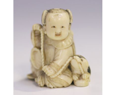 A Japanese carved ivory netsuke, Meiji period, modelled as a seated child accompanied by a puppy, incised and black stained t