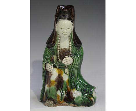 A Chinese famille verte enamelled biscuit porcelain figure of Guanyin, Kangxi period, modelled kneeling wearing a long volumi