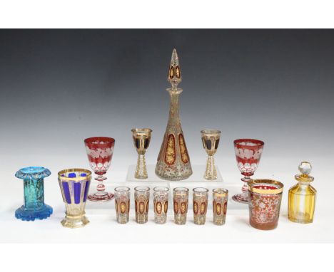 A Bohemian ruby flashed and enamelled glass liqueur set, early 20th century, each piece with a ruby ground oval panel gilt wi