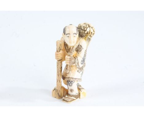 Japanese Meiji period carved ivory netsuke, in the form of a man with a basket of food over his shoulder and holding a staff,