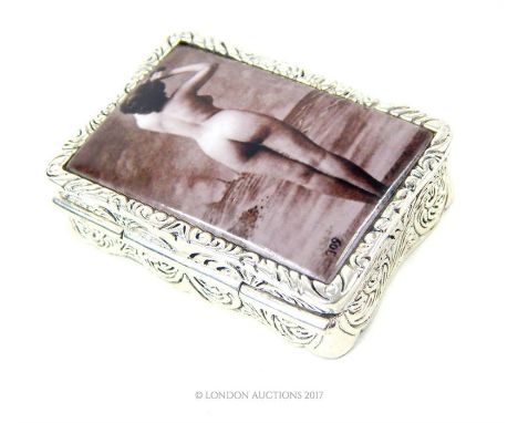 A white metal pill box with an enamel image of a standing female nude; 5cm long.