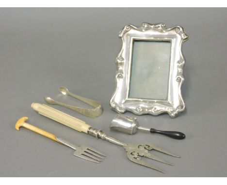 A silver photograph frame, a pair of sugar tongs, a silver shovel, a toasting fork with ivory handle, and another modelled as