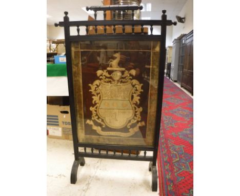 A late Victorian ebonised fire screen in the aesthetic manner with needlework panel of an armorial inscribed "Prudentia et Pe