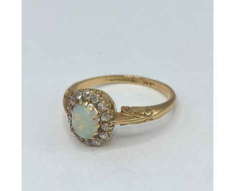 A 18ct gold opal ring surrounded by fourteen diamonds, having scroll shaped shoulders Size N 1/2. 3.4g 