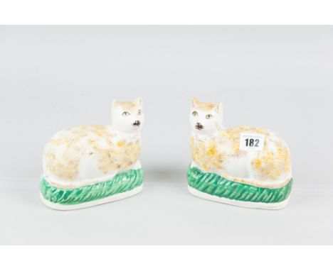 A pair of Staffordshire pottery models of recumbent cats opposing figures, with ochre colour spongeware decoration on green p