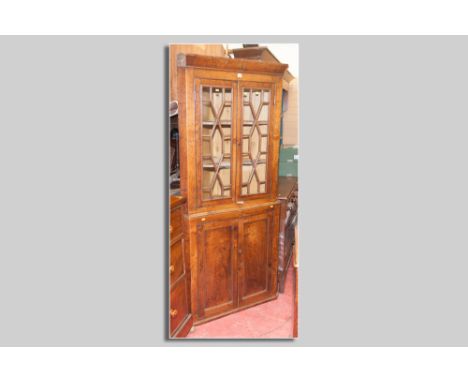 A Georgian oak and elm two piece corner cupboard, the top with chamfered cornice above twin thirteen panel glazed doors with 