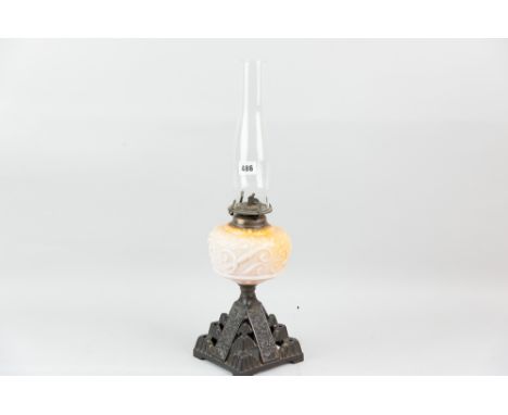 An iron based oil lamp with yellow tinted milk glass reservoir and chimney