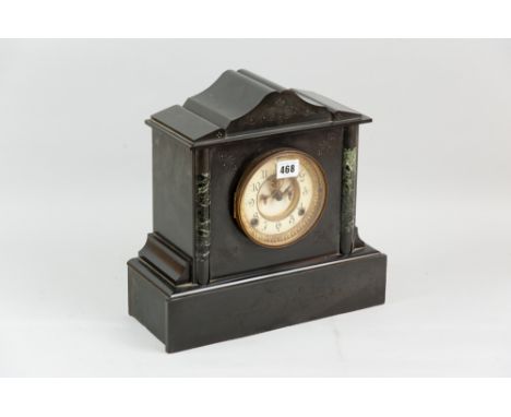 A black slate oblong based mantel clock with green mottled pillars either side of the circular dial with visible escapement, 