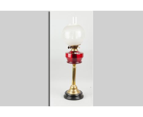 A brass based oil lamp with cranberry glass reservoir and etched bowl shade
