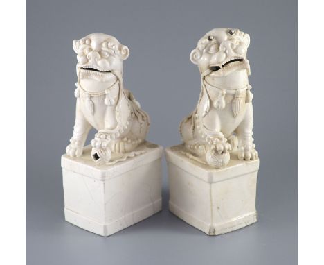   A pair of Chinese Dehua blanc de chine Buddhist lion joss stick holders, Kangxi period,each standing with one paw on a broc