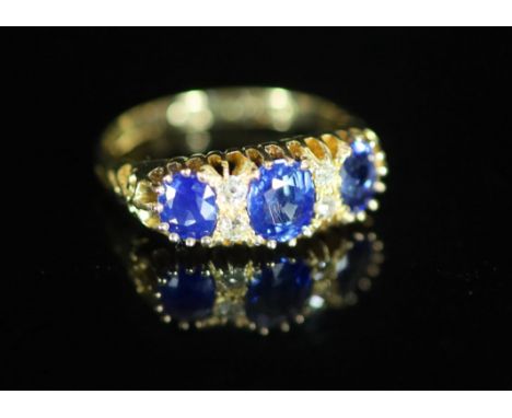   An Edwardian 18ct gold and three stone sapphire set half hoop ring with diamond chip spacers,with carved shoulders, size M,