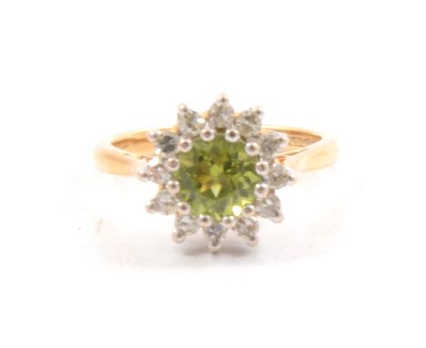 A peridot and diamond circular cluster ring, the 6mm round brilliant cut peridot claw set and surrounded by twelve eight cut 