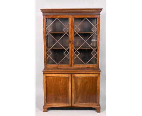 A late Georgian mahogany bookcase shelved and enclosed by astragal glazed doors under a dentil moulded cornice on a cupboard 