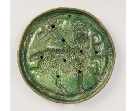 A Medieval pottery circular plaque, green glazed, pierced and moulded with the Lamb of God and supported on three short stub 