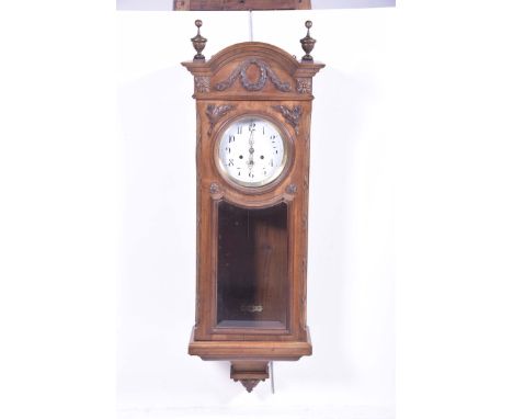 An early 20th Century walnut cased wall clockWith an arched pediment above a 7" enamel dial painted with Arabic numerals, hav