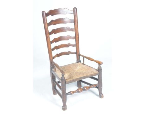 An 18th Century elm ladder back low seat chairThe six rung back above an envelope rush seat flanked by turned arm rests, rais