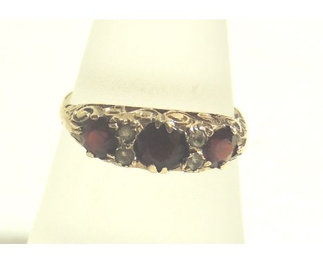 A 9ct gold ladies dress ring set with three red stones, possibly garnets, separated with small clear stones in a decorative p