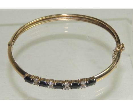 A 9ct gold hinged bangle, set with five dark sapphires, each spaced by a pair of white stones.   