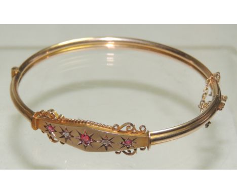 A 9ct gold bangle, the central lozenge panel set with central red stone, flanked by two small diamonds and then two smaller r