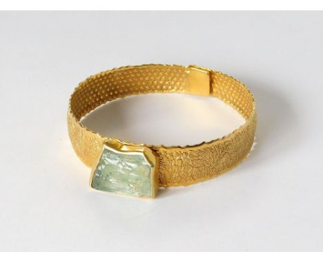HAND MADE BANGLE. A Corfiot (Corfu) 18ct. gold (unstamped) textured bangle, set an irregularly shaped natural aquamarine ston
