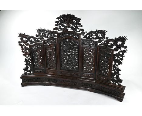 A decorative Chinese hardwood five-panel table screen, profusely carved and pierced with designs of fierce dragons disputing 